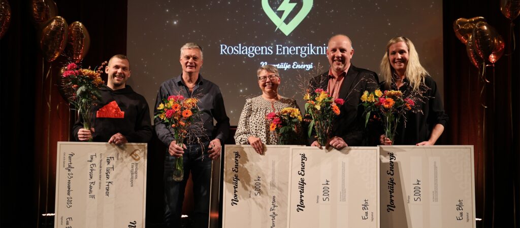 Fem personer med blommor och stora checkar på prisutdelning.