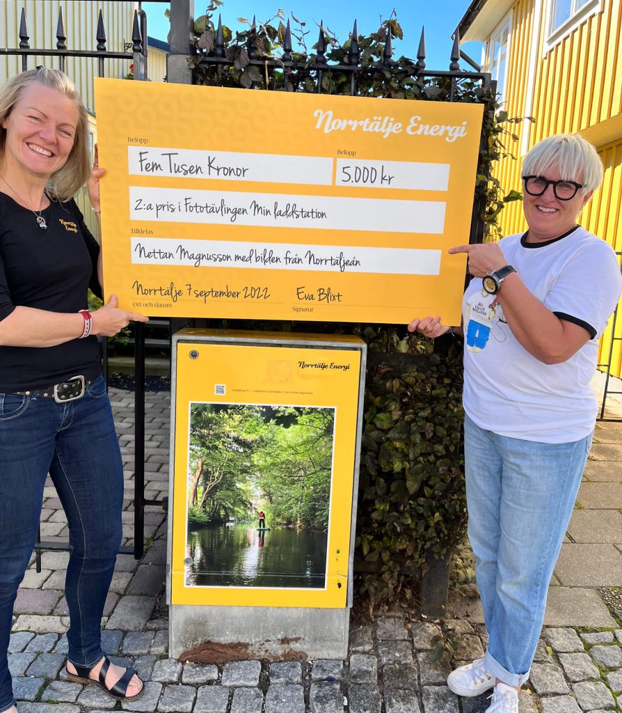 En kvinna (vinnare) och Eva, chef Norrtälje Energi med en check på 10.000 kr, fototävling "Min laddstation".