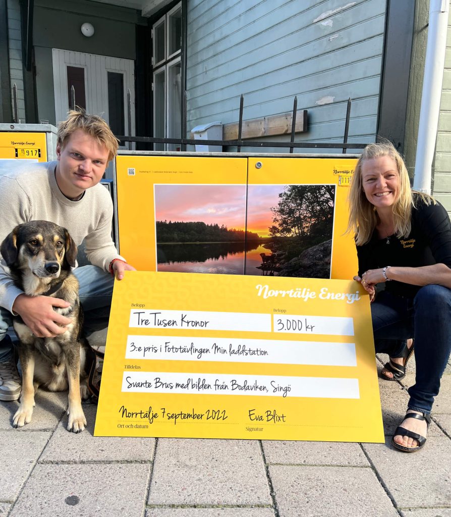 En man och sin hund (vinnare) och Eva, chef Norrtälje Energi med en check på 10.000 kr, fototävling "Min laddstation".