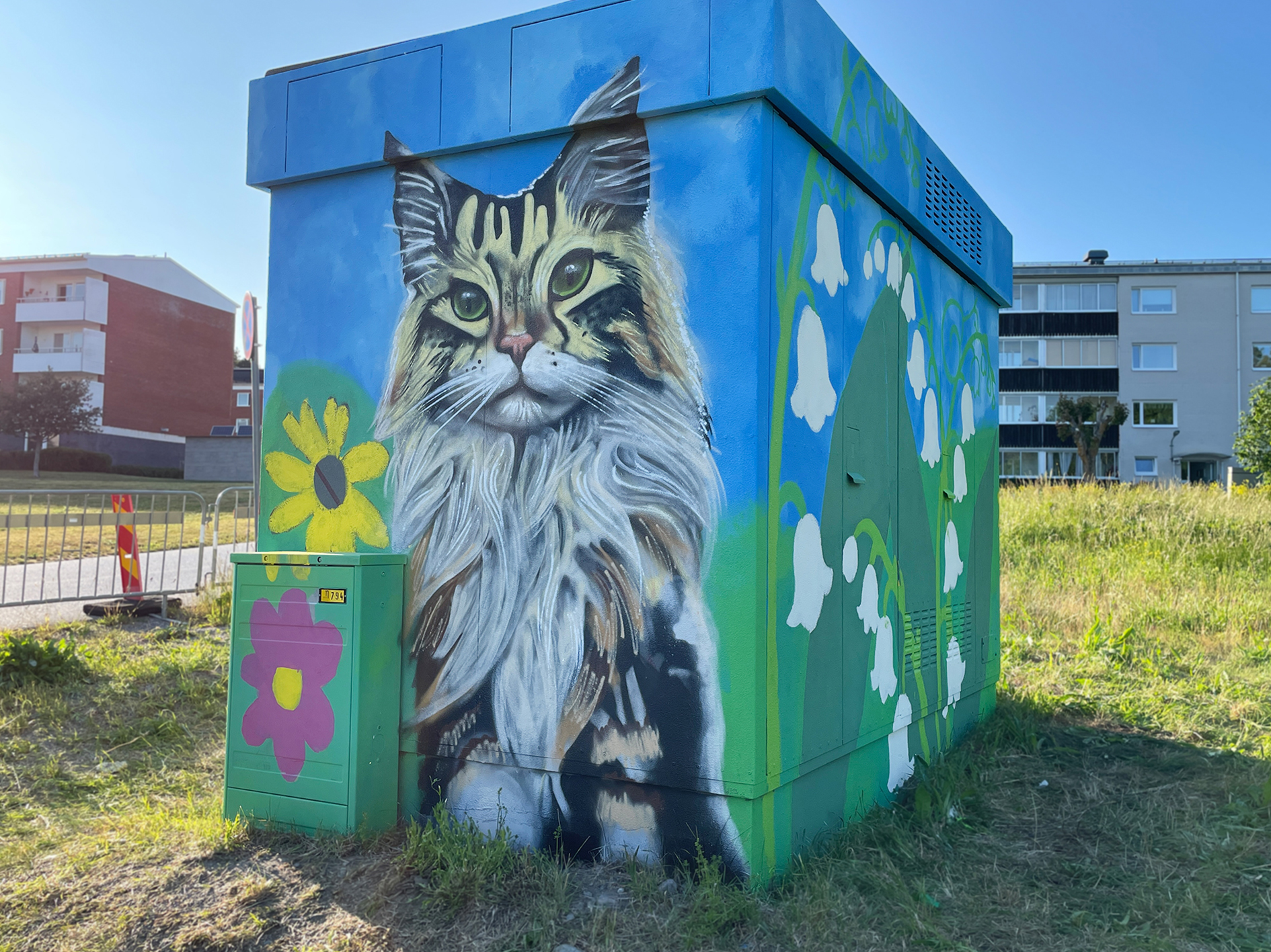 Ett elskåp dekorerat med ett detaljerat porträtt av en långhårig katt med grön bakgrund och blå himmel.