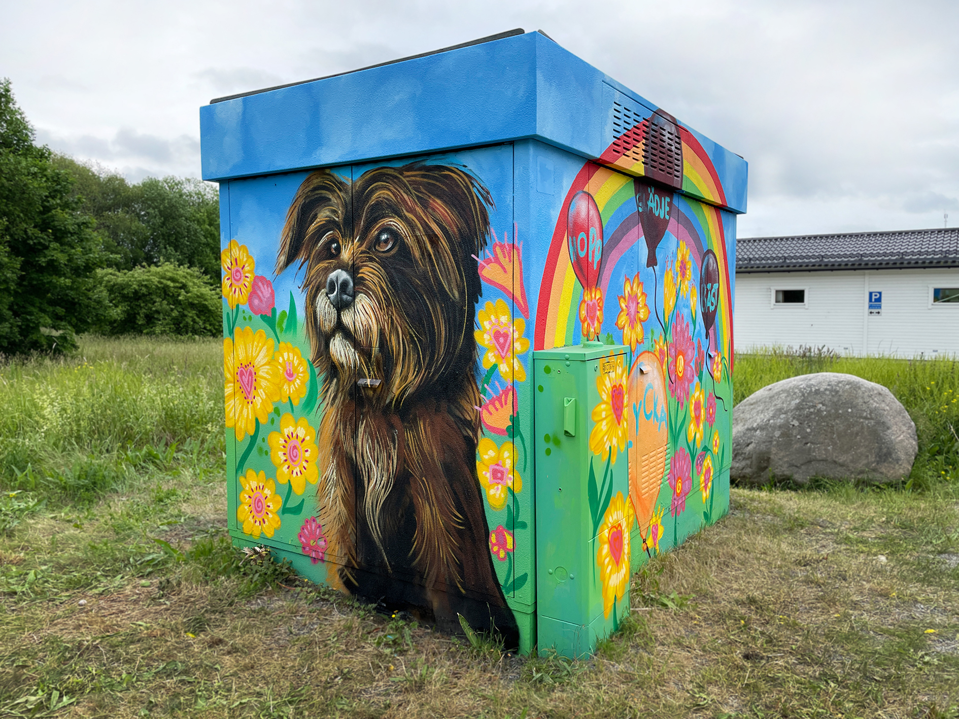 Målning på ett elskåp föreställande en hund omgiven av färgglada blommor.