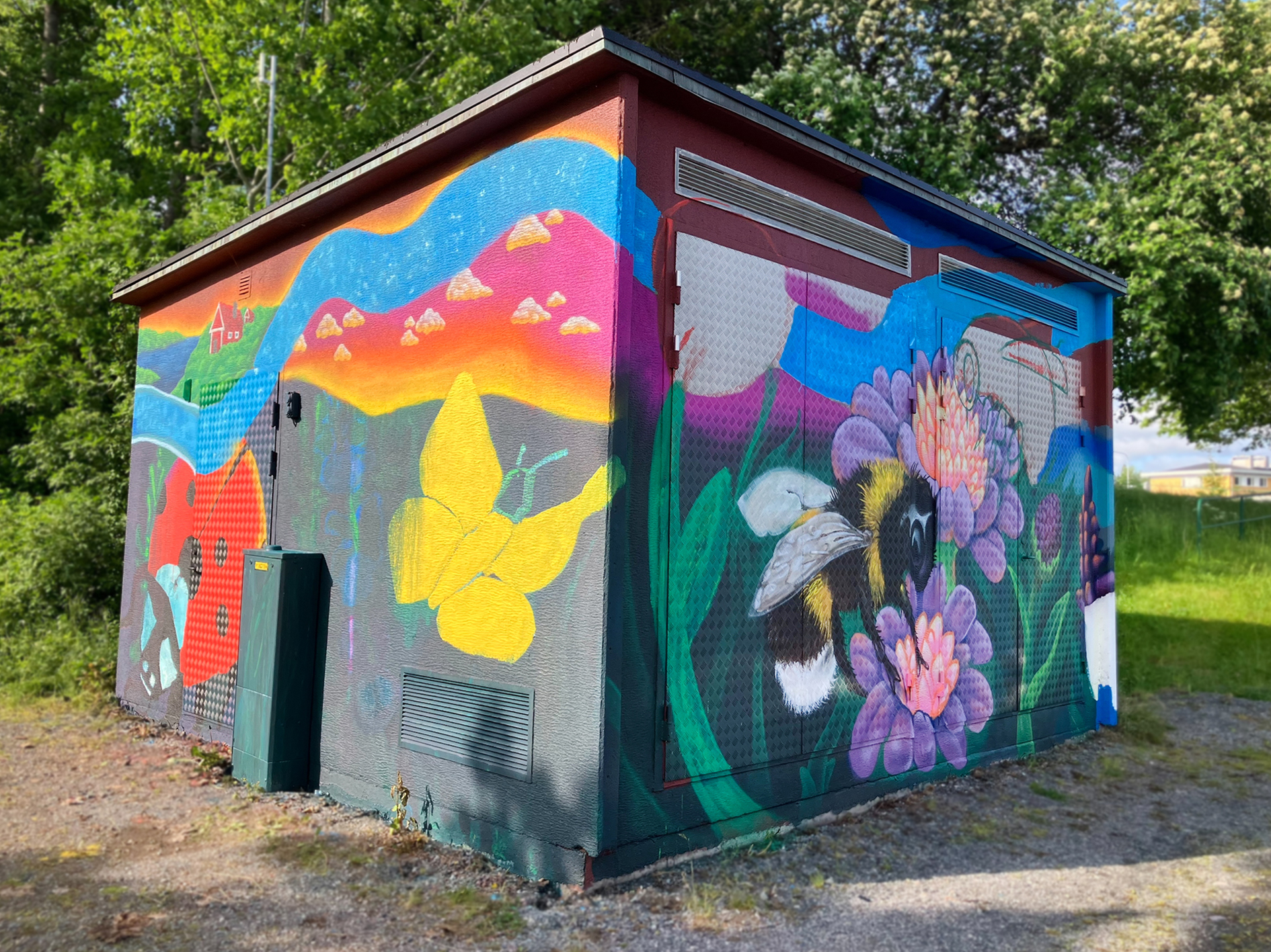 En liten byggnad, troligtvis ett teknikhus eller elskåp, är täckt av en färgstark muralmålning.