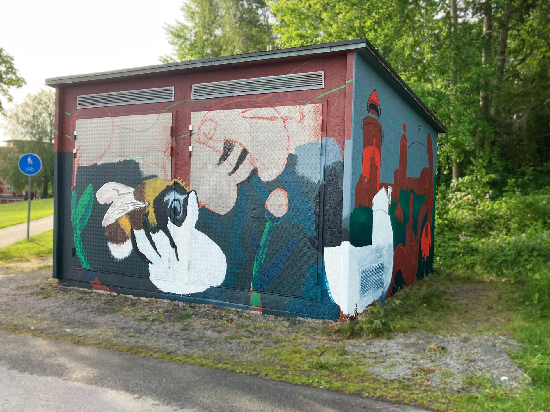 En nätstation med en påbörjad väggmålning. Motivet inkluderar en realistiskt målad humla på en vit blomma till vänster.