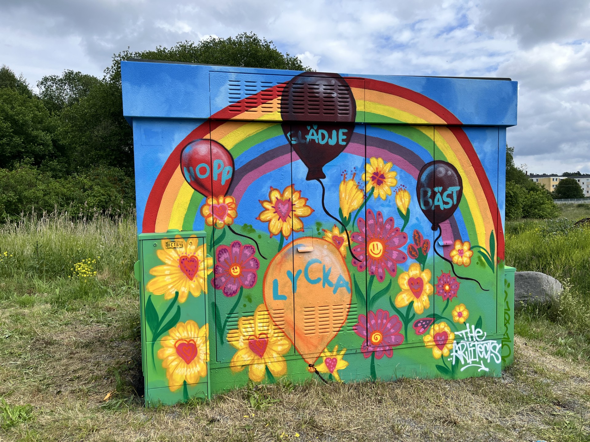 En elnätsstation är målad med färgglad gatukonst som föreställer blommor, hjärtan, ballonger och en regnbåge.