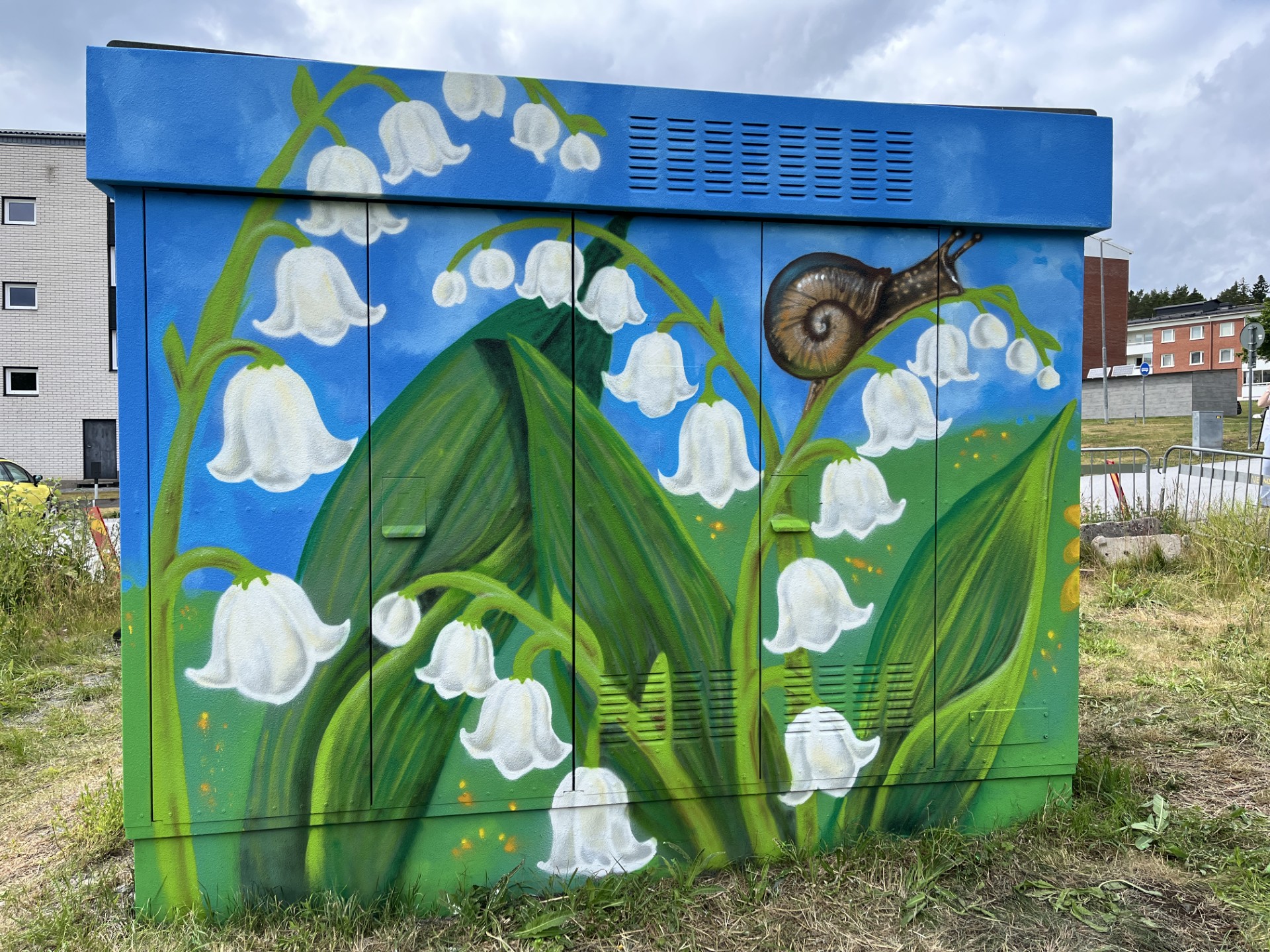 En elnätsstation är målad med färgglad gatukonst som föreställer lillekonvaljer.