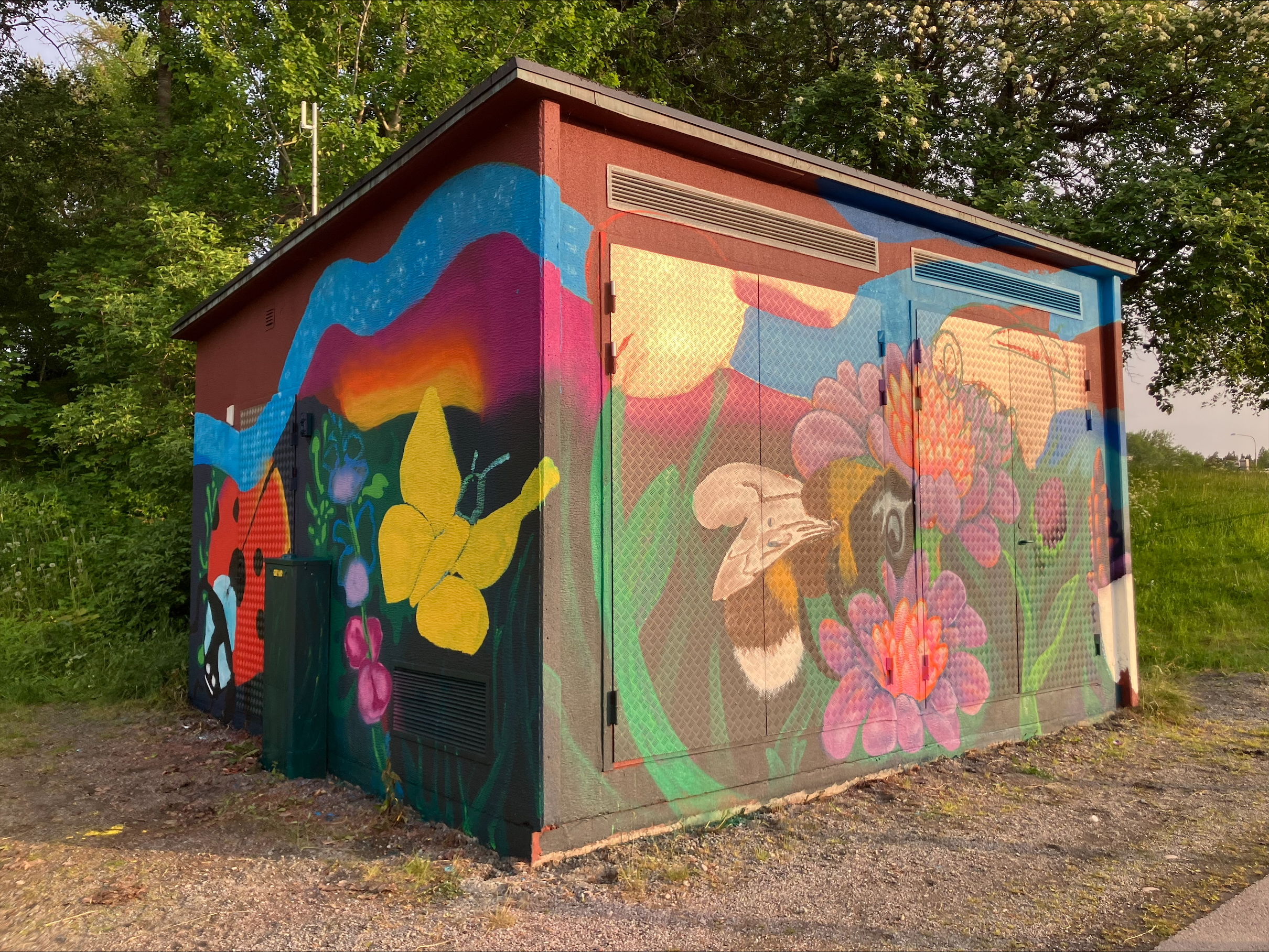 En liten byggnad, troligen ett elskåp eller teknikskjul, är täckt av färgglad gatukonst.