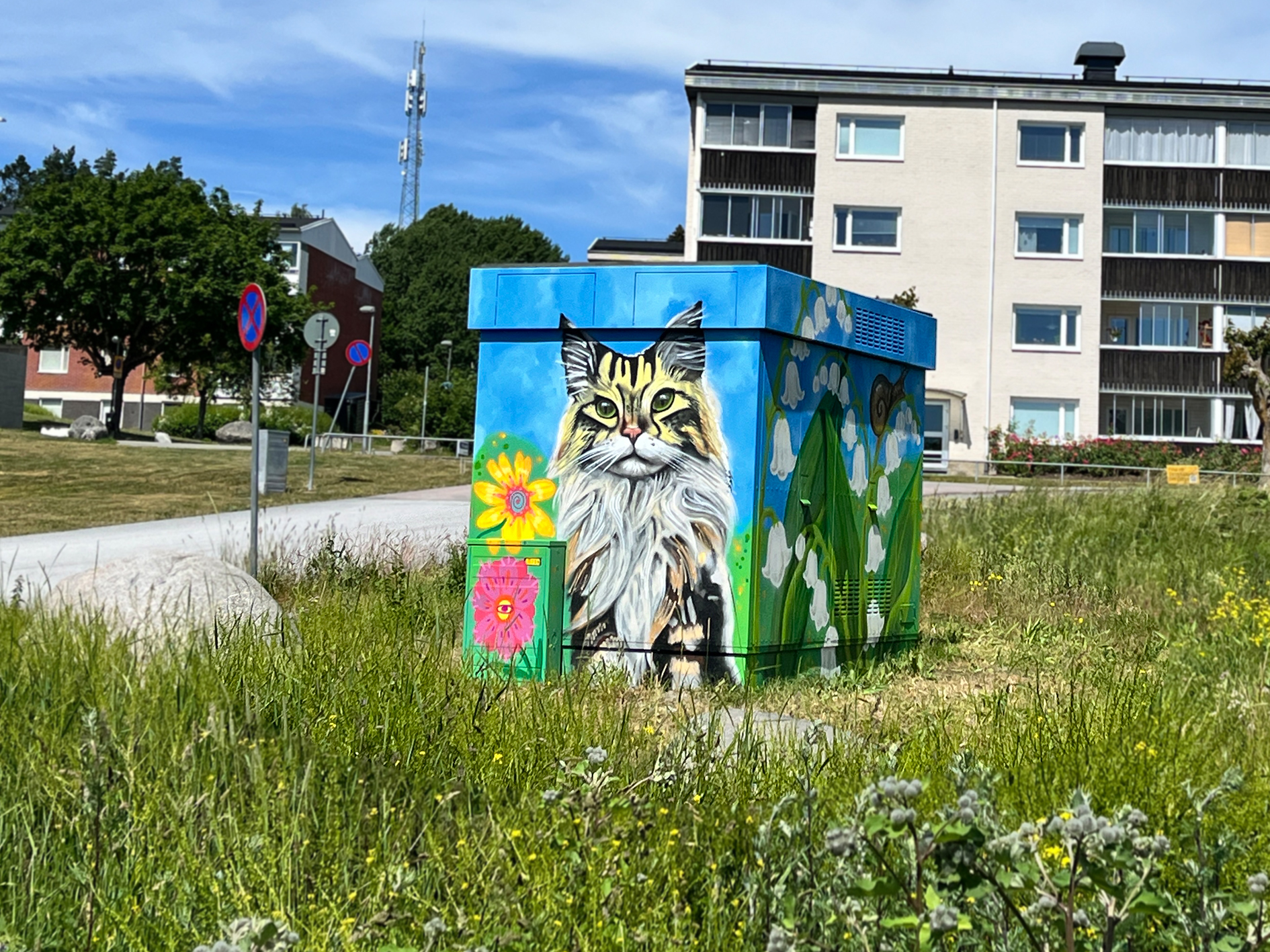 Elskåp målat med en katt, blommor och liljekonvaljer i ett bostadsområde.