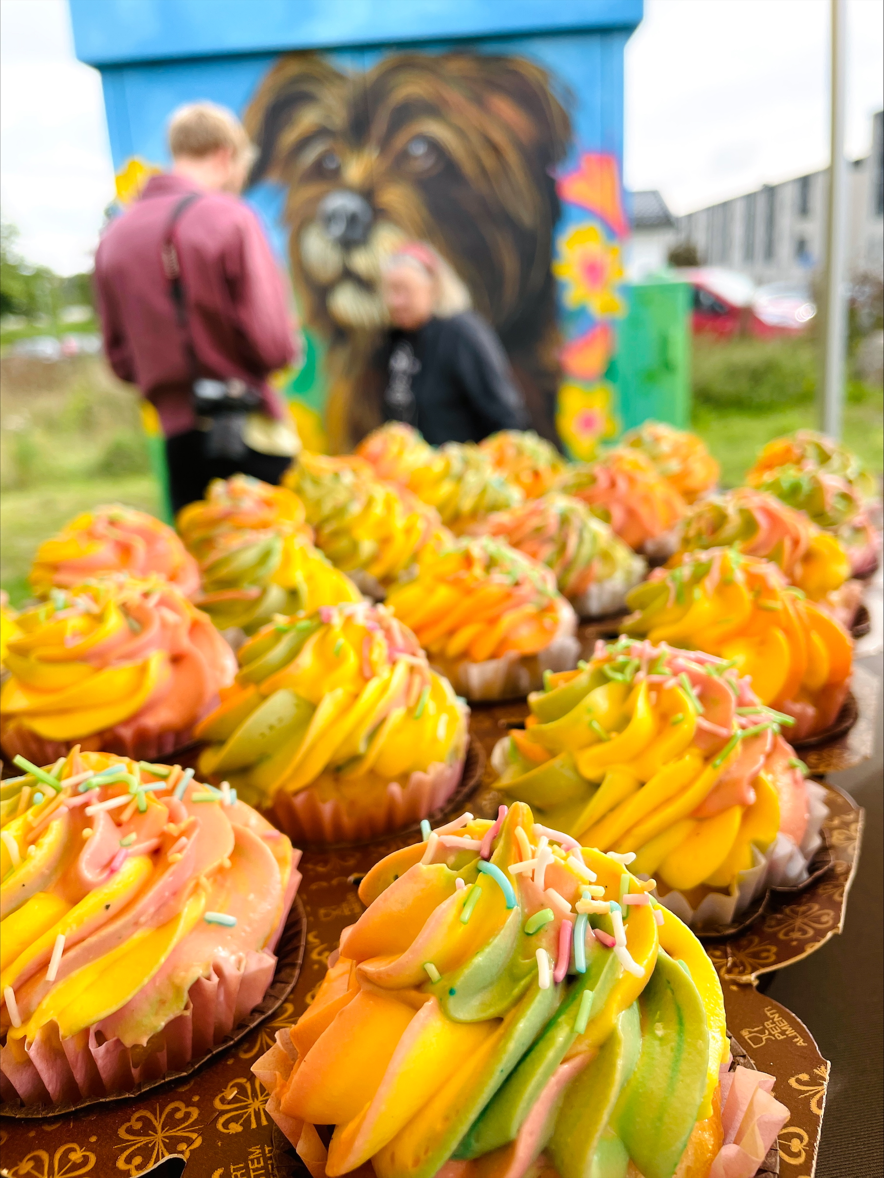 Färgglada cupcakes framför muralmålning med hundmotiv.