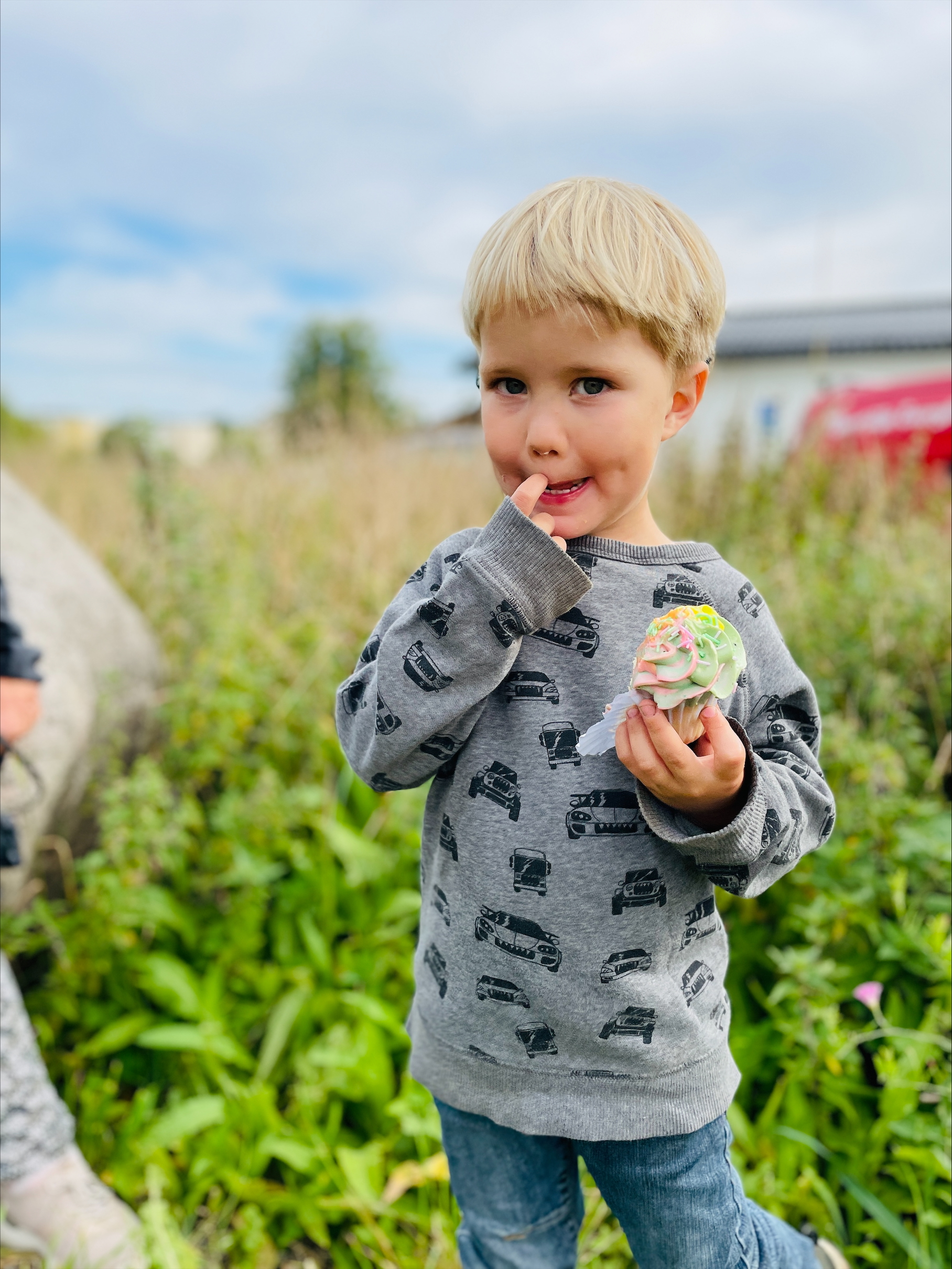 Barn äter cupcake utomhus på gräsfält.