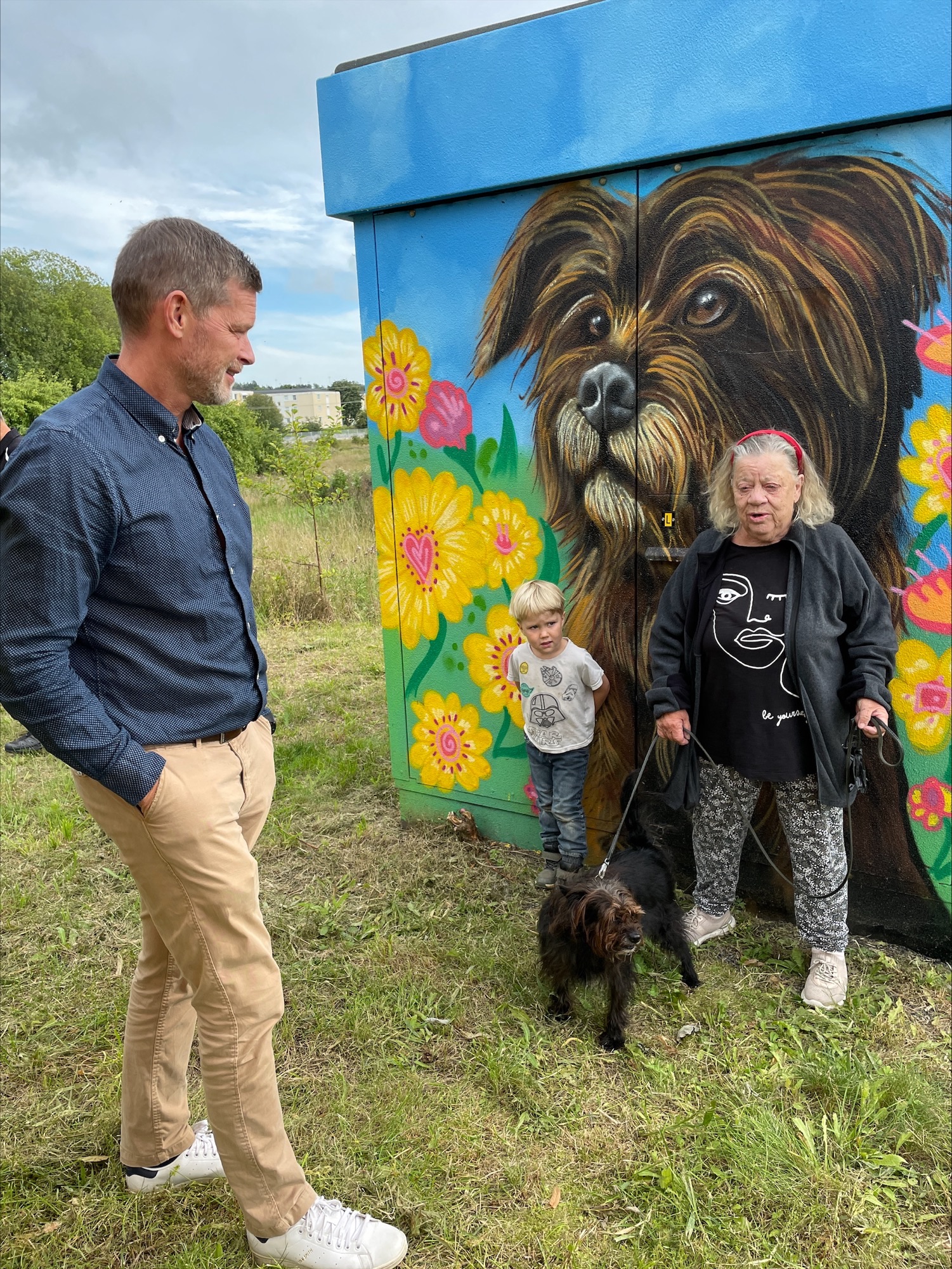 Personer och hund framför muralmålning av hund med blommor.