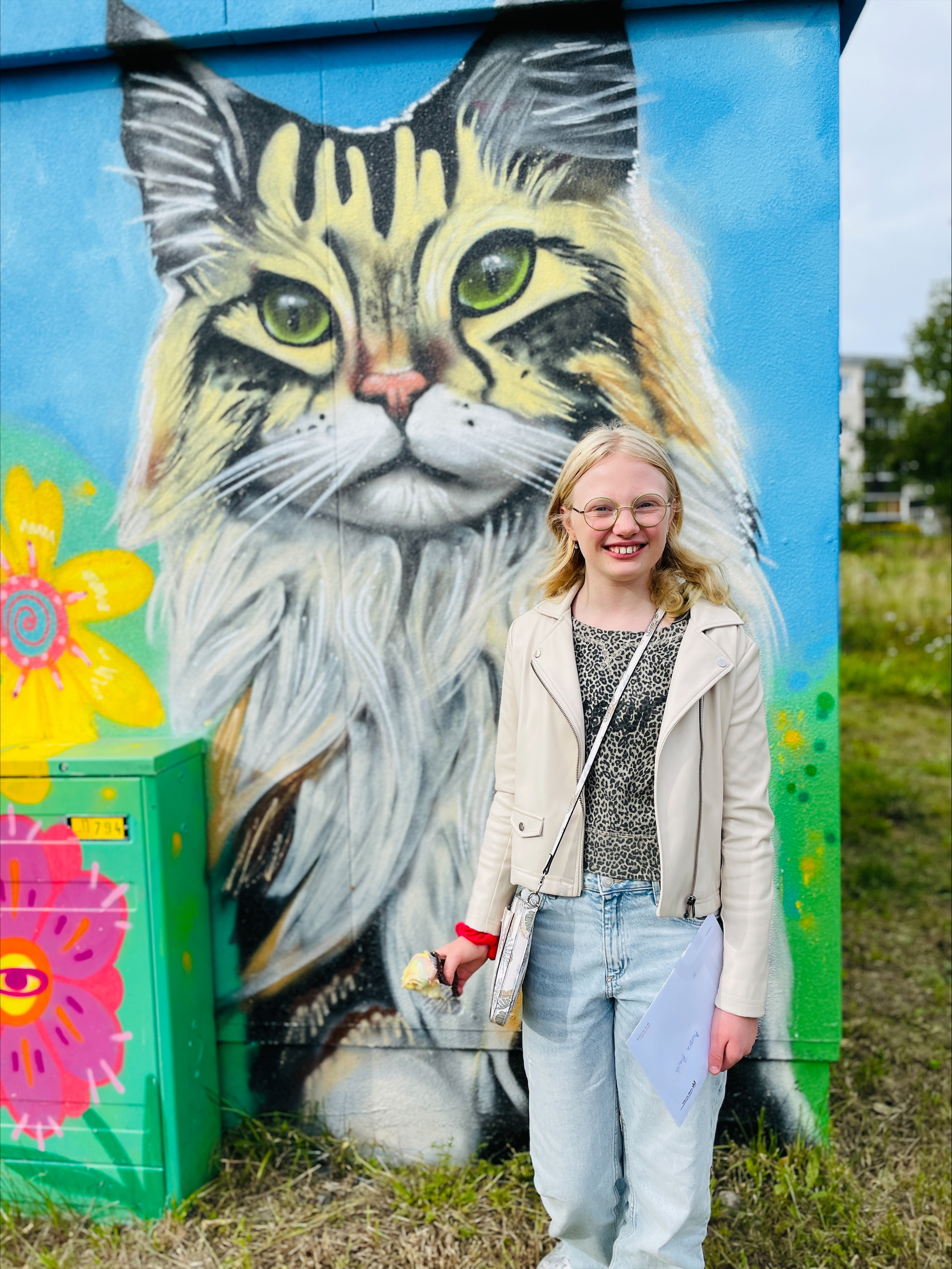 Person framför muralmålning av katt med blommor.