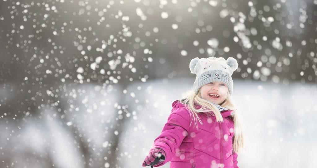 Barn i rosa vinterjacka leker i snöfall och skrattar.