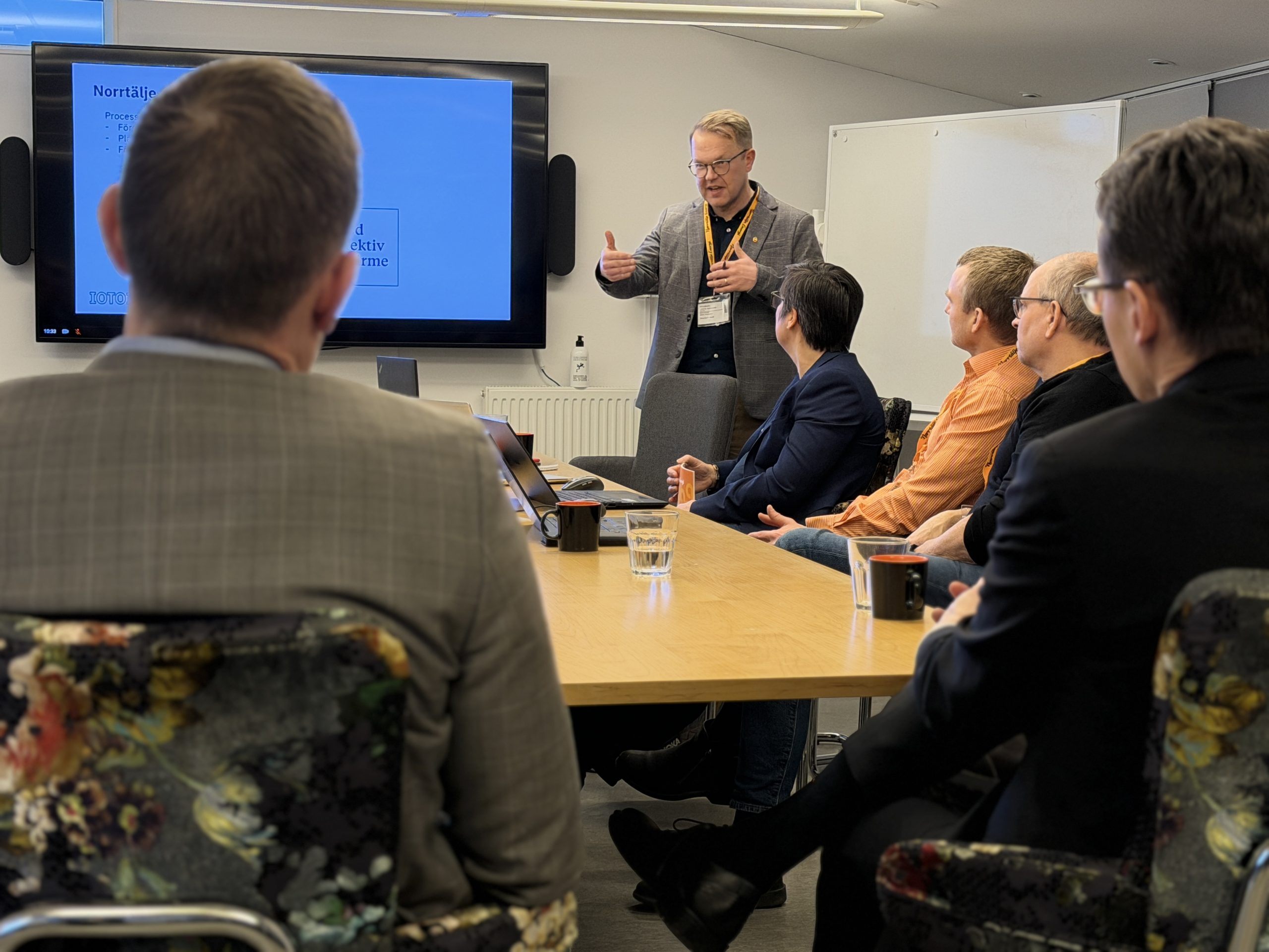Person presenterar vid möte framför skärm i konferensrum.