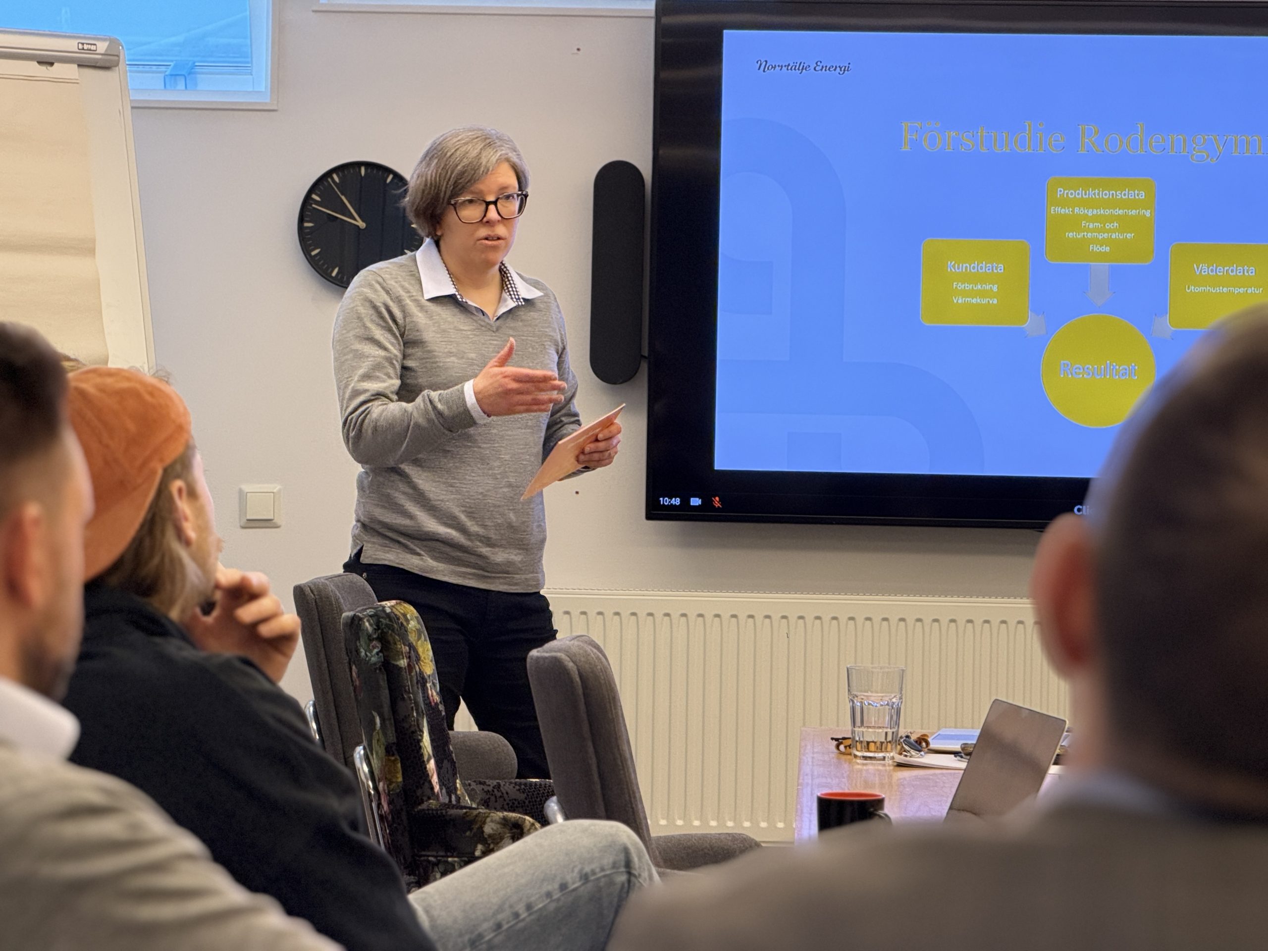 Kvinna presenterar vid möte framför skärm i konferensrum.