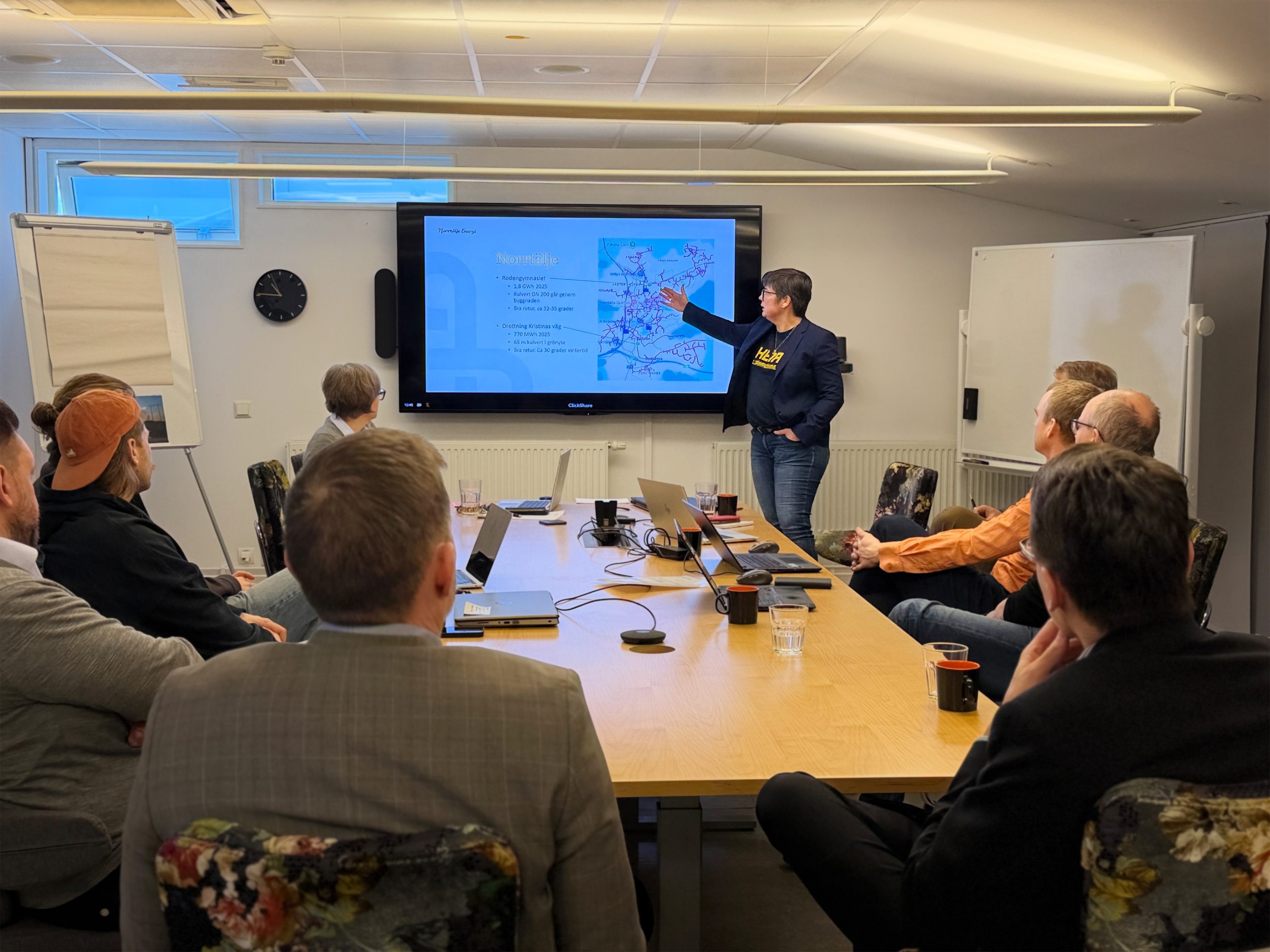 Kollega presenterar vid möte framför skärm i konferensrum.