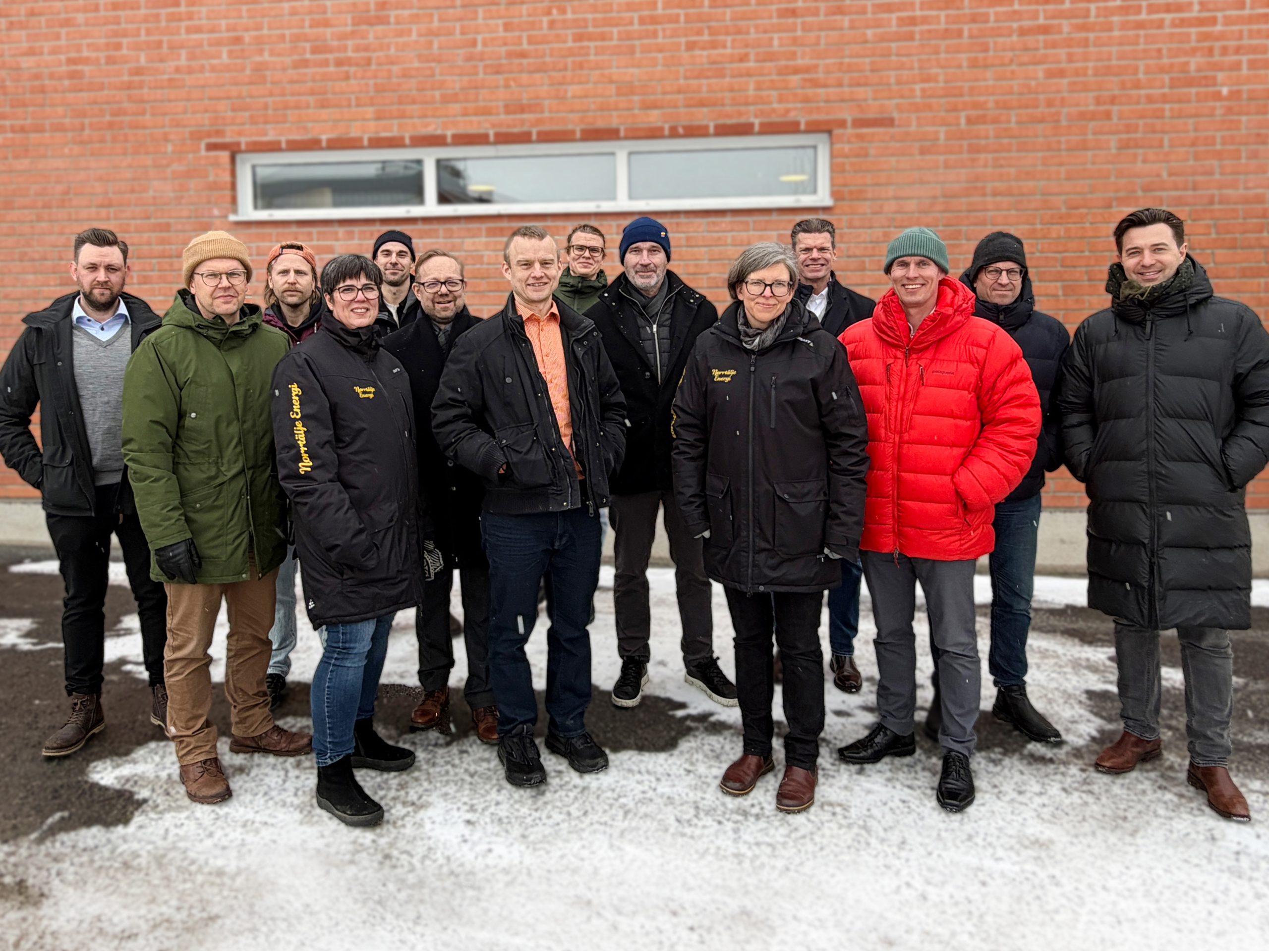 Grupp personer i vinterkläder framför tegelvägg utomhus