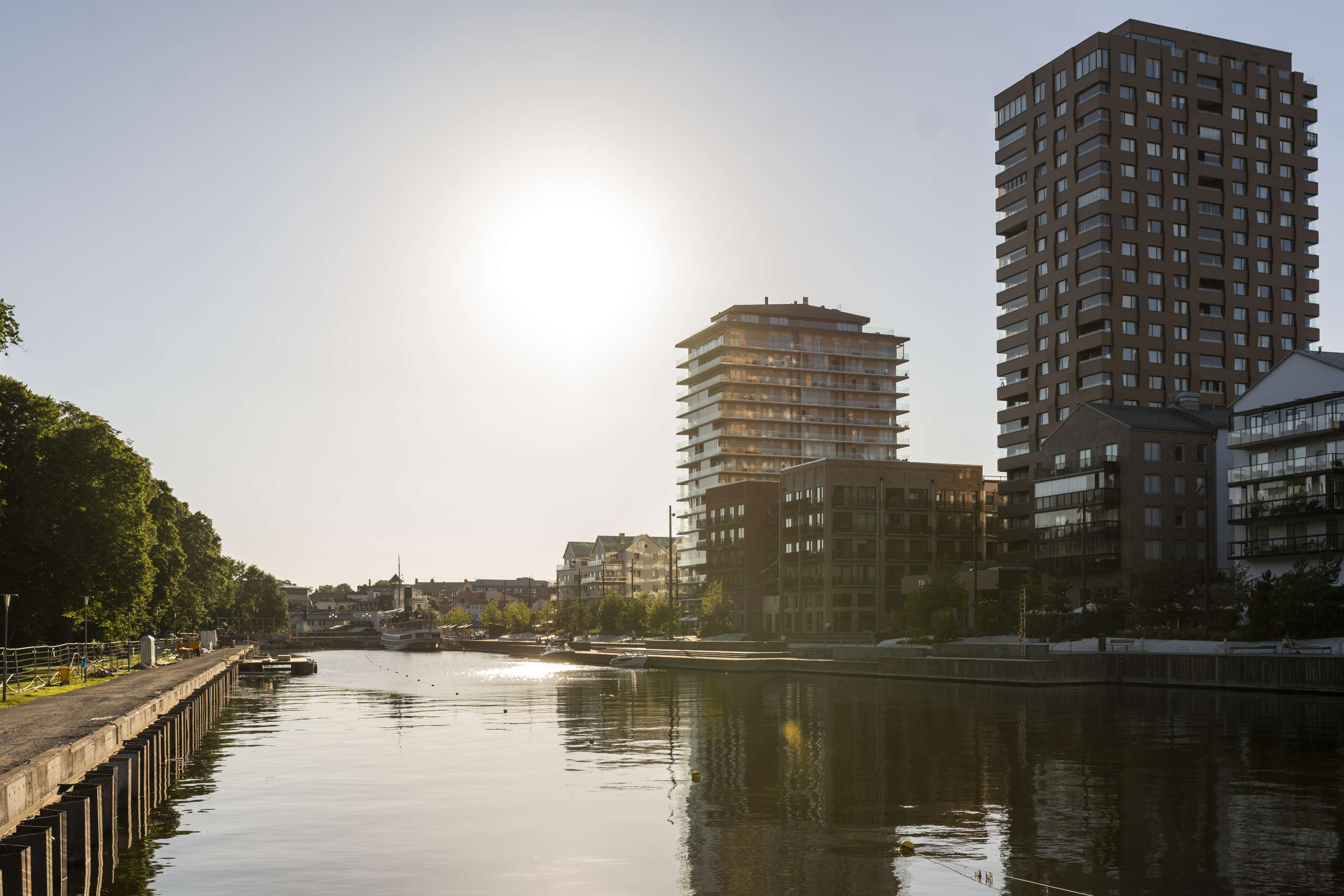 Sol över å med höghus, speglingar i vattnet.